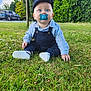 Liam a rejoint le concours — aidez-le/la à gagner de superbes lots ! baby, child, grass, outdoor, pacifier, cap, blue_eyes, overalls, shirt, sitting, greenery, trees, car, nature, daylight, cute, infant, young_child, casual_clothing, portrait