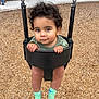 Jerzain Eden joined the competition — help win amazing prizes! toddler, child, swing, playground, curly_hair, green_socks, black_swing, wood_chips, outdoor, park, bench, person, grass, sidewalk, casual_clothing, hands, legs, face, expression, daytime