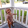 Octavius joined the competition — help win amazing prizes! toddler, child, porch, wooden_floor, white_railing, striped_clothing, smiling, happy, outdoor, daylight, grass, residential_area, car, stop_sign, curly_hair, playful, person, casual_wear, motion_blur, urban