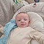 baby, infant, onesie, baby_nest, blanket, couch, soft_texture, smile, face, head, person, indoor, cozy, comfort, child, young, cute, resting, blue_blanket, beige_clothing