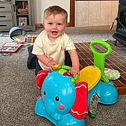 Grant is registered to the contest to win money with this photo: toddler, child, toy, elephant_toy, indoor, carpet, cabinet, book, play, smile, person, furniture, floor, plastic_toy, colorful, seat, wooden, happy, room, baby
