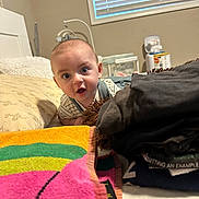 Matteo is registered to the contest to win money with this photo: baby, infant, bed, blanket, clothing, folded_clothes, face, furniture, indoor, mattress, person, portrait, room, towel, window, window_blinds, young_child, curtains, pillow, toy