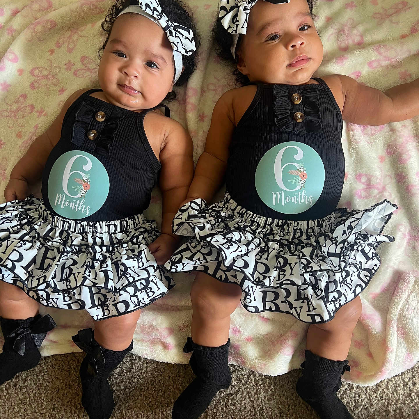 Amelie And Brielle is registered to the contest to win money with this photo: baby, twins, infant, six_months, headband, black_clothing, ruffled_skirt, socks, blanket, pink, butterfly_pattern, curly_hair, lying_down, carpet, cute, portrait, two_children, indoor, smiling, adorable