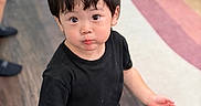 Jerome joined the competition — help win amazing prizes! toddler, child, indoor, floor, black_tshirt, checkered_pants, curly_hair, looking_up, person, young_child, wooden_floor, rug, cute, casual_clothing, standing, expression, portrait, small_child, short_hair, skin