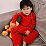 barefoot, black_hair, casual, child, couch, cozy, curious_expression, cute, home, indoors, pajamas, plush_toy, portrait, red_clothing, relaxed, sitting, sofa, teddy_bear, toddler, young_child