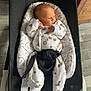 baby, newborn, infant, bouncer, baby_bouncer, baby_seat, onesie, patterned_clothing, harness, buckle, soft_cushion, wooden_floor, flooring, indoor, portrait, side_gaze, hand_near_face, legs, cozy, parenthood
