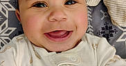 Sir' Hunter is registered to the contest to win money with this photo: baby, blanket, child, closeup, clothing, cute, expression, face, happy, head, indoor, infant, lying_down, onesie, pattern, portrait, skin, small_person, smiling, soft_toy