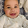 baby, blanket, child, closeup, clothing, cute, expression, face, happy, head, indoor, infant, lying_down, onesie, pattern, portrait, skin, small_person, smiling, soft_toy