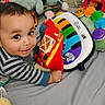 baby, bed, child, colorful, cushion, cute, face, hand, happy, indoor, infant, person, piano, play, plush, smile, soft_toy, striped_clothing, toy, young