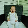 baby, infant, smile, happy, sitting, chair, wicker, cushion, white_clothing, overalls, animal_design, face, hands, feet, porch, outdoor, wall_siding, child, cute, young
