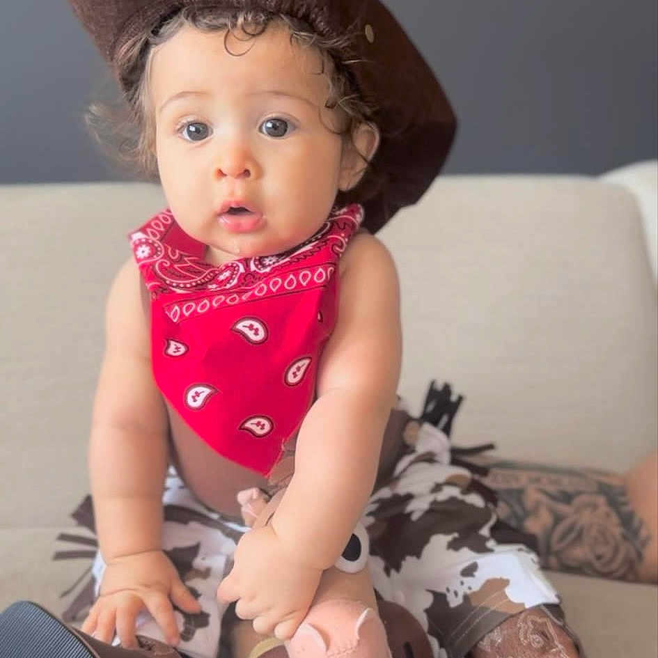 James is registered to the contest to win money with this photo: accessories, baby, bonnet, clothing, couch, cushion, dress, face, footwear, furniture, hat, head, headband, people, person, photography, portrait, shoe, sitting, sleeve
