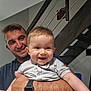 baby, child, man, smile, happy, holding, watch, arm, indoor, staircase, railing, shirt, person, face, skin, hair, expression, home, bonding, family