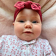 Emery is registered to the contest to win money with this photo: baby, infant, headband, red_bow, onesie, floral_pattern, pink_blanket, soft_texture, face, cheeks, eyes, portrait, cute, child, lying_down, indoors, closeup, expression, adorable, clothing