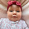 baby, infant, headband, red_bow, onesie, floral_pattern, pink_blanket, soft_texture, face, cheeks, eyes, portrait, cute, child, lying_down, indoors, closeup, expression, adorable, clothing