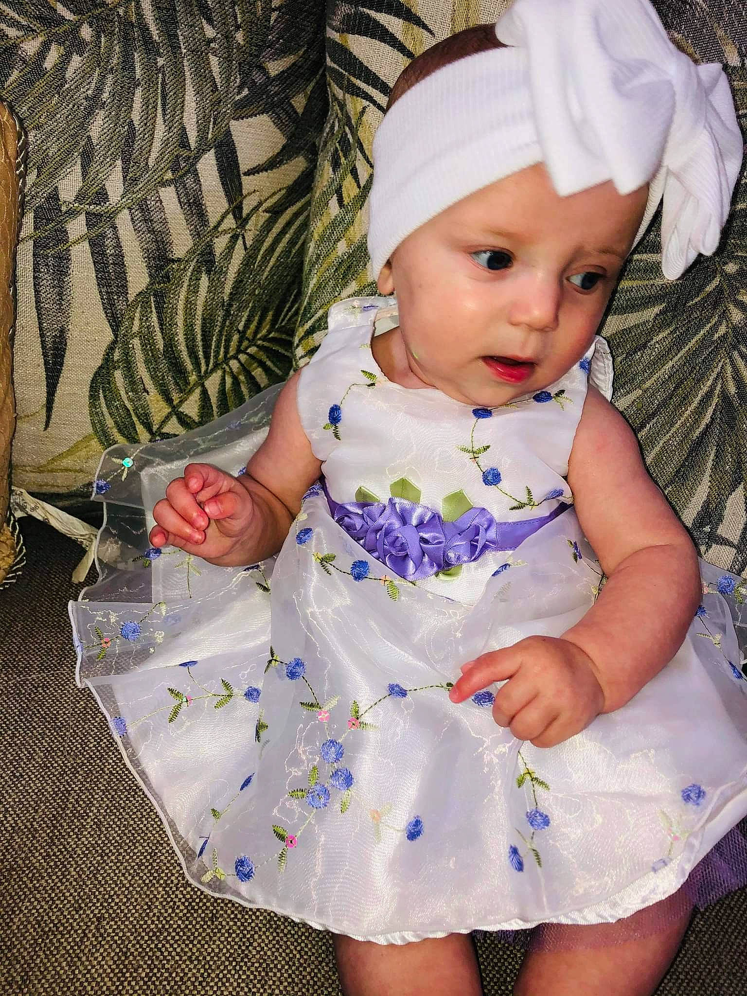 Avery is registered to the contest to win money with this photo: baby, baby_toddler_clothing, child, day_dress, dress, embellishment, facial_expression, grass, headwear, iris, one_piece_garment, pattern, person, pink, product, purple, sitting, skin, sleeve, textile