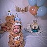 baby, child, teddy_bear, costume, birthday, cake, balloons, party_hat, plush_toys, celebration, smiling, sitting, portrait, indoors, decorations, number_six, sprinkles, blanket, festive, photography
