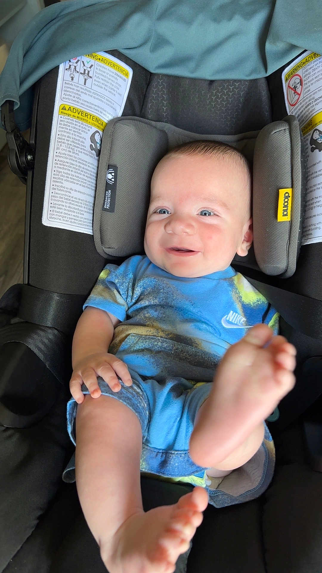 Silas is registered to the contest to win money with this photo: baby, child, car_seat, smile, happy, blue_clothing, nike, feet, infant, head_support, seat_belt, indoor, person, cute, young_child, playful, skin, face, hand, foot