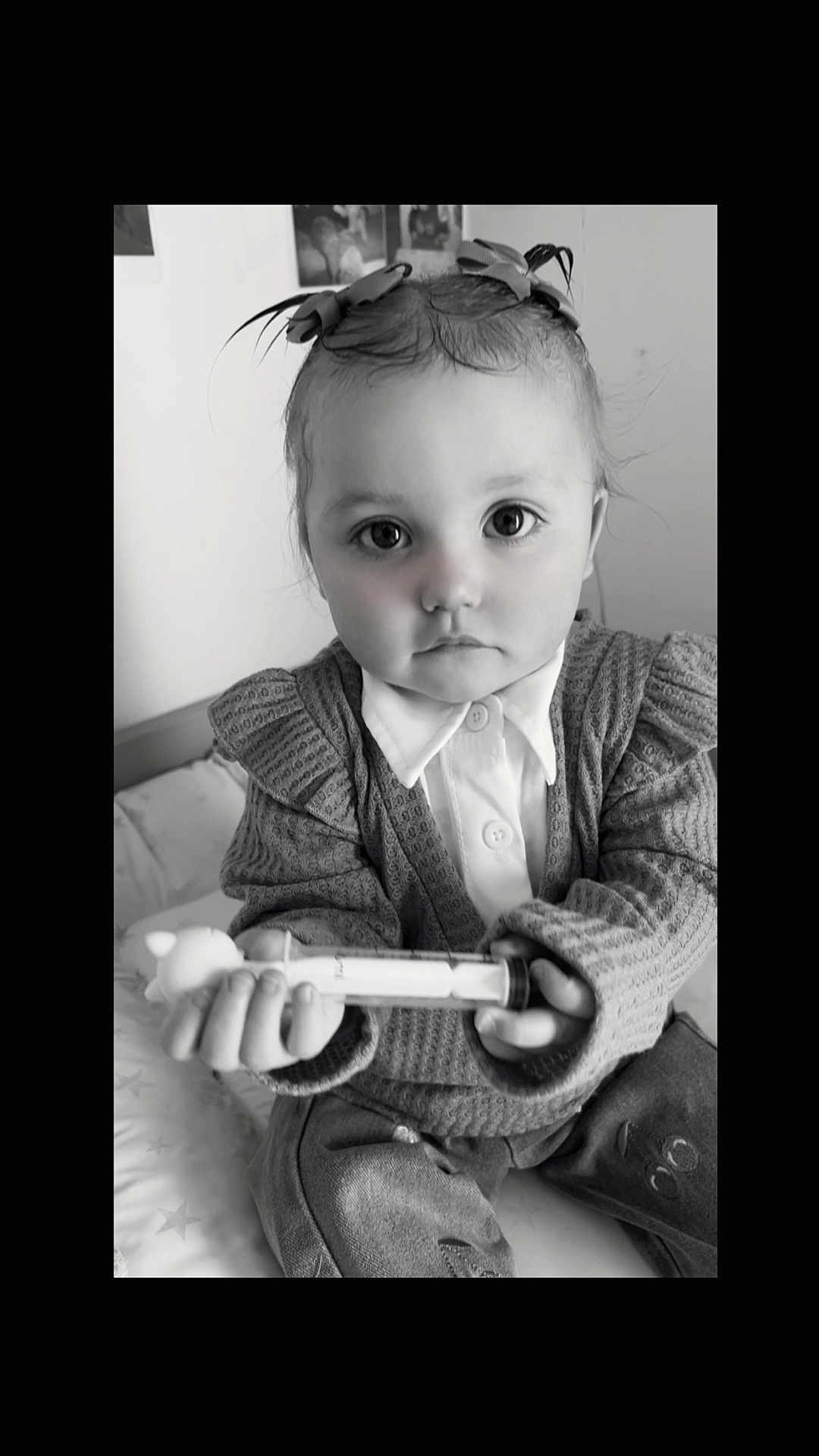 Leewena participe au concours pour gagner de l'argent avec cette photo : child, baby, toddler, portrait, black_and_white, big_eyes, hair_bows, sweater, collared_shirt, buttons, hands, toy, syringe, bed, blanket, indoor, closeup, serious_expression, cute, sitting