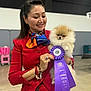 Barbie is registered to the contest to win money with this photo: accessories, award, bracelet, celebration, competition, dog, fluffy, happy, holding, indoor, pet_show, pomeranian, portrait, puppy, red_clothing, ribbon, ring, scarf, smile, woman