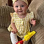 baby, child, yellow_dress, headband, toy_gun, couch, indoor, smiling, sitting, cute, portrait, furniture, infant, happy, person, clothing, legs, feet, hand, face