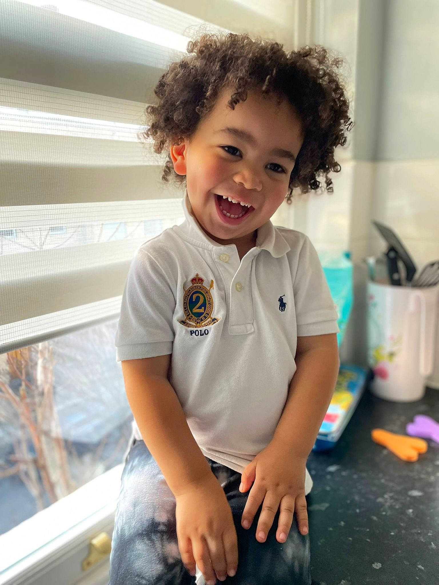 Ezra is registered to the contest to win money with this photo: baby_toddler_clothing, child, elbow, electric_blue, eye, face, flooring, fun, happy, head, knee, person, play, sitting, sleeve, smile, t_shirt, toddler, top, travel