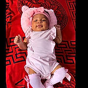 Ellia is registered to the contest to win money with this photo: baby, infant, pink_clothing, hat, socks, lying_down, blanket, red, versace, cute, smiling, child, portrait, indoors, baby_accessories, headwear, fabric, soft, comfortable, one_person