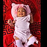 baby, infant, pink_clothing, hat, socks, lying_down, blanket, red, versace, cute, smiling, child, portrait, indoors, baby_accessories, headwear, fabric, soft, comfortable, one_person