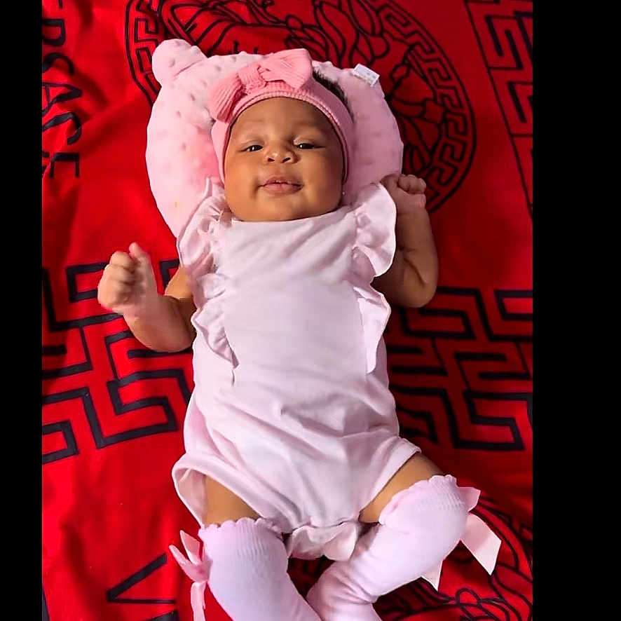 Ellia is registered to the contest to win money with this photo: baby, infant, pink_clothing, hat, socks, lying_down, blanket, red, versace, cute, smiling, child, portrait, indoors, baby_accessories, headwear, fabric, soft, comfortable, one_person