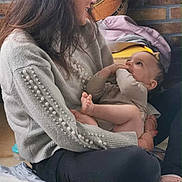 Andrea a rejoint le concours — aidez-le/la à gagner de superbes lots ! woman, baby, brick_wall, blanket, indoor, casual_clothing, smiling, child, person, floor, home, couch, long_hair, sitting, holding, footwear, socks, cozy, interaction, happy