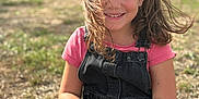 Layana a rejoint le concours — aidez-le/la à gagner de superbes lots ! child, girl, smile, outdoor, grass, hair, pink_shirt, black_overalls, sitting, sunlight, bracelet, happy, portrait, nature, daylight, casual_clothing, person, young, background_blur, wind