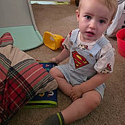 Sawyer is registered to the contest to win money with this photo: bucket, carpet, child, clothing, curious, floor, furniture, home, indoor, light_blond_hair, person, plaid_blanket, shirt, shorts, sitting, sock, superman_logo, toddler, toy, yellow_toy