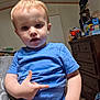 toddler, child, blue_shirt, indoor, person, furniture, dresser, clutter, toy_box, face, hand, light_hair, curious, casual, home, room, carpet, adult_hand, expression, portrait