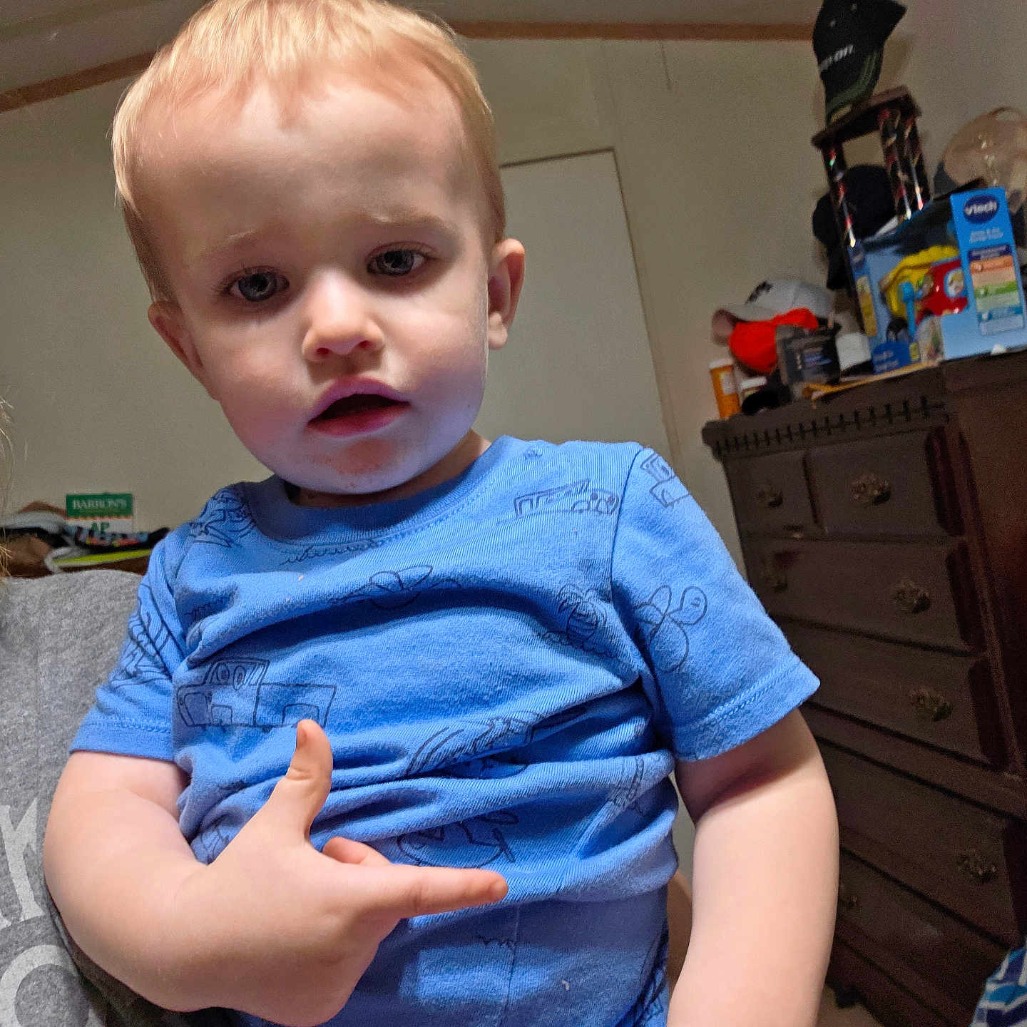 Sawyer is registered to the contest to win money with this photo: adult_hand, blue_shirt, carpet, casual, child, clutter, curious, dresser, expression, face, furniture, hand, home, indoor, light_hair, person, portrait, room, toddler, toy_box