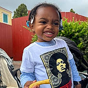 Riley joined the competition — help win amazing prizes! casual_clothing, child, daylight, expression, french_fry, graphic_tee, greenery, hair_clips, happy, holding_food, outdoor, person, playful, portrait, red_fence, smiling, stroller, tshirt, watch, young_child