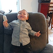 John a rejoint le concours — aidez-le/la à gagner de superbes lots ! child, toddler, smile, brush, armchair, couch, denim_shirt, button_up, happy, indoor, living_room, furniture, portrait, hair, tooth, playful, blanket, tile_floor, printer, chair