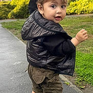 Gurnawab Singh is registered to the contest to win money with this photo: toddler, child, person, boots, jacket, vest, hand, sidewalk, grass, building, outdoor, curious, walking, brown_hair, clothing, face, eyes, urban, daylight, holding_hand