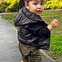 toddler, child, person, boots, jacket, vest, hand, sidewalk, grass, building, outdoor, curious, walking, brown_hair, clothing, face, eyes, urban, daylight, holding_hand