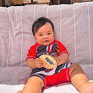 James joined the competition — help win amazing prizes! baby, child, infant, red_clothing, towel, plaque, milestone, smiling, portrait, indoors, ceiling_fan, stone_wall, striped, feet, hands, cute, sitting, person, home, casual