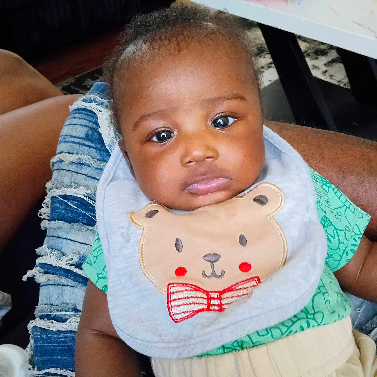 Jervontaye is registered to the contest to win money with this photo: baby, child, person, bib, clothing, denim, jeans, indoor, table, bottle, face, expression, sitting, lap, hand, green, beige, cute, infant, casual