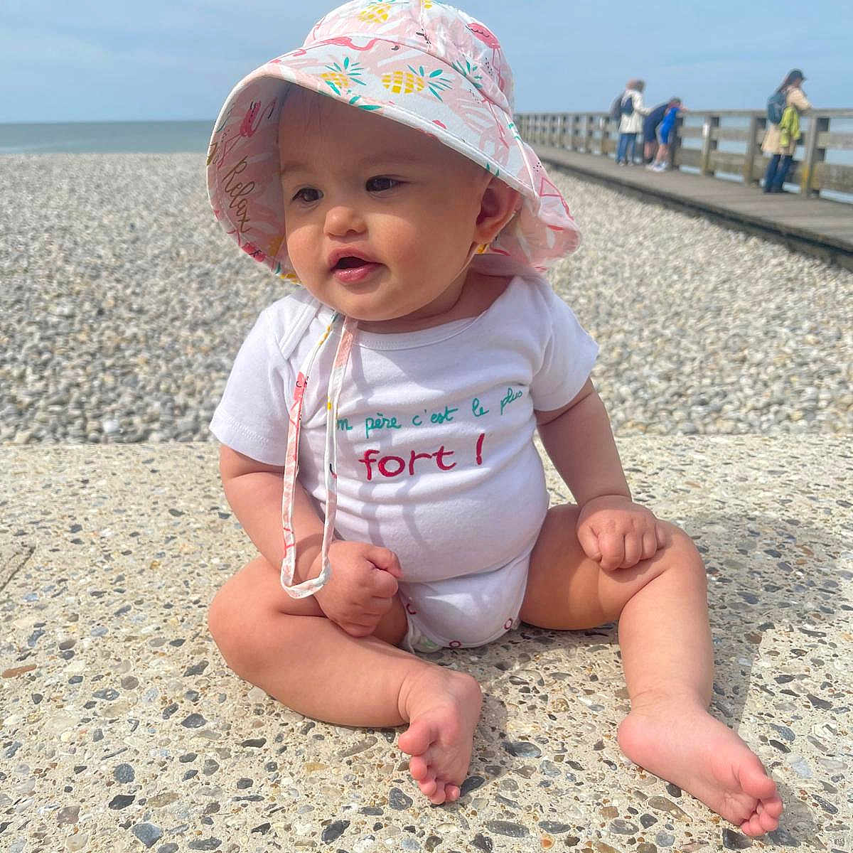 Emma participe au concours pour gagner de l'argent avec cette photo : baby, beach, beachwear, clothing, coast, face, hat, head, nature, outdoors, person, photography, pier, portrait, sea, shoreline, sitting, summer, water, waterfront