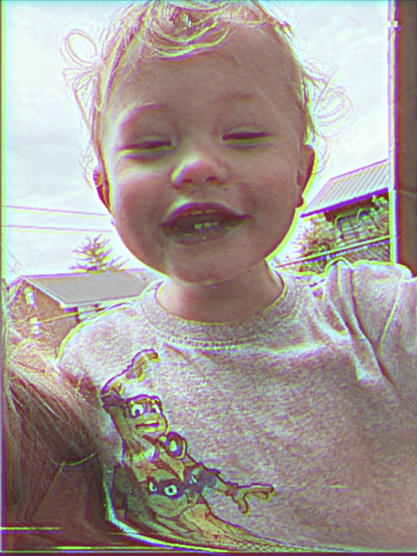 Tate is registered to the contest to win money with this photo: toddler, child, smiling, curly_hair, grey_shirt, animated_character, outdoor, house, greenery, daylight, portrait, happy, person, casual_clothing, closeup, cute, young_child, expression, funny_face, playful
