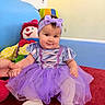 Sophie is registered to the contest to win money with this photo: baby, child, purple_tutu, headband, smiling, sitting, hand_holding, doll, plush_toy, carpet, indoor, colorful, cute, portrait, toddler, clothing, footwear, soft_toys, playroom, happy
