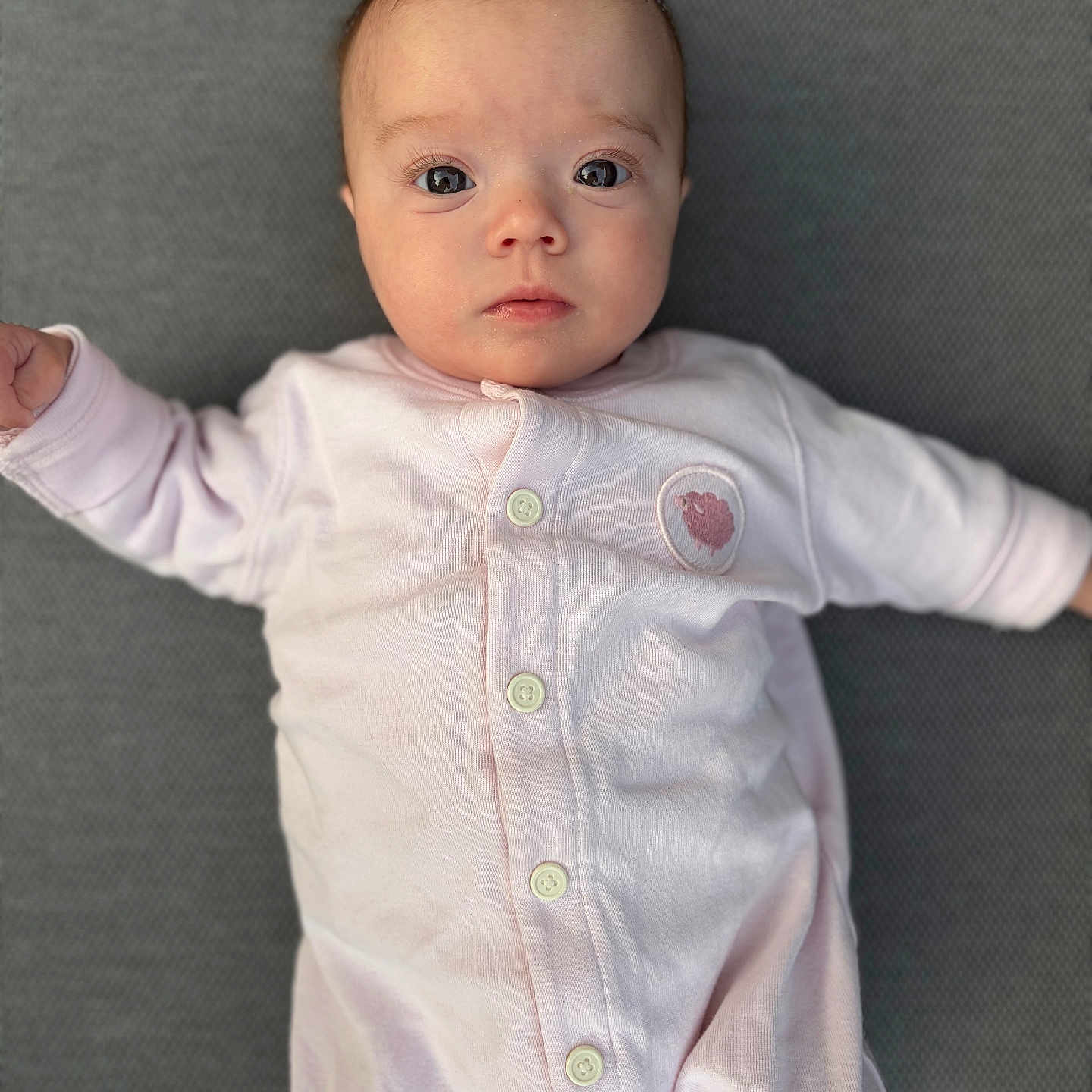 Anna participe au concours pour gagner de l'argent avec cette photo : baby, infant, onesie, pink_clothing, face, eyes, buttoned_clothing, lying_down, texture, gray_background, portrait, cute, young_child, small_hands, soft_fabric, looking_at_camera, skin, head, expression, close_up