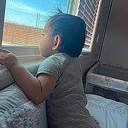 Elijah joined the competition — help win amazing prizes! toddler, child, window, looking_out, striped_clothing, onesie, indoors, bed, blanket, curtains, natural_light, hair, playpen, baby, side_profile, hand, furniture, room, curiosity, soft_light