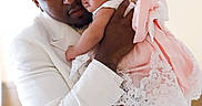 Kehlani is registered to the contest to win money with this photo: man, baby, child, holding, embrace, white_suit, pink_dress, bow, lace, indoor, affection, love, portrait, family, people, cute, tender, headband, infant, closeup