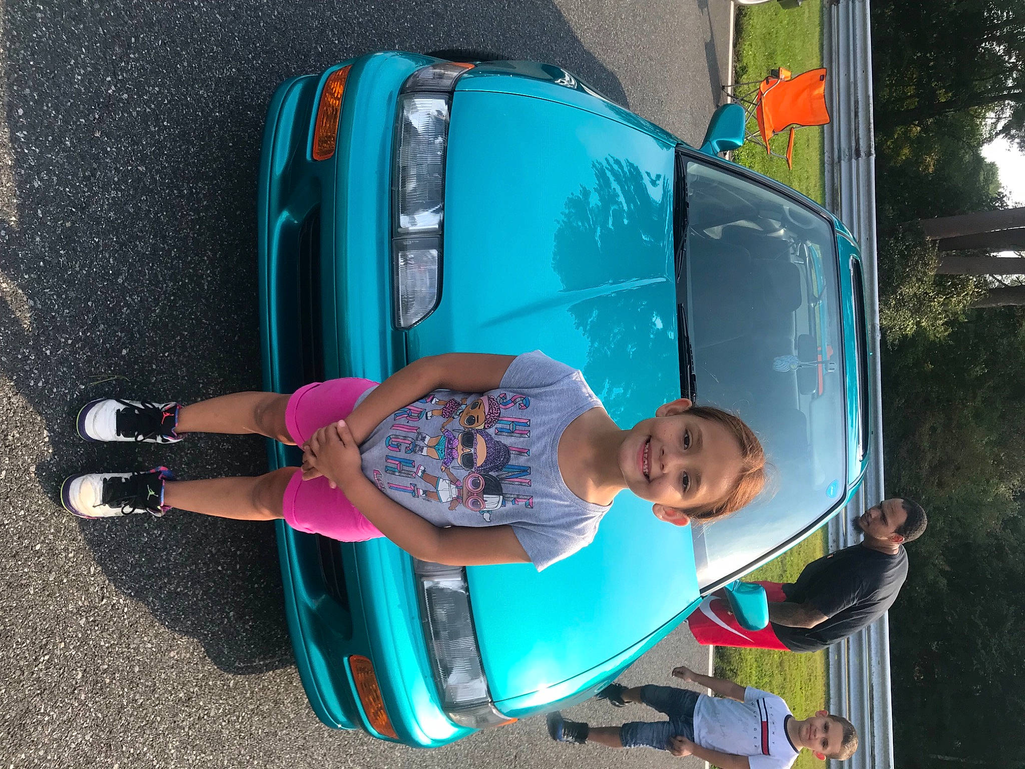 Jessenia is registered to the contest to win money with this photo: automotive_design, automotive_exterior, automotive_lighting, blue, bumper, car, electric_blue, hood, joy, leisure, motor_vehicle, person, recreation, smile, t_shirt, tire, toddler, tree, trunk, vehicle