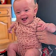 Madlyne a rejoint le concours — aidez-le/la à gagner de superbes lots ! baby, smiling, infant, person, hand, clothing, indoor, kitchen, cabinet, adult, holding, happy, cute, skin, face, sitting, patterned_clothing, expression, child, human