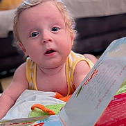 Maxime participe au concours pour gagner de l'argent avec cette photo : baby, child, curly_hair, blue_eyes, book, reading, blanket, indoor, living_room, curious, infant, soft_toys, yellow_clothing, close_up, portrait, toddler, couch, comfort, playtime, expression