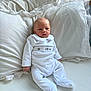 baby, infant, bed, pillow, white_clothing, onesie, sleepwear, indoor, newborn, cute, resting, soft, blanket, comfort, portrait, person, child, young, cozy, peaceful