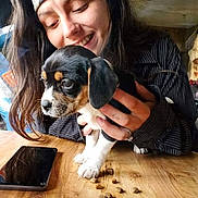 Pocahontas is registered to the contest to win money with this photo: brown_black_white, casual_clothing, cute, dog, dog_food, domestic, friendly, hands, happy, headband, indoor, long_hair, pet, puppy, smartphone, smiling, table_surface, woman, wooden_table, young_adult